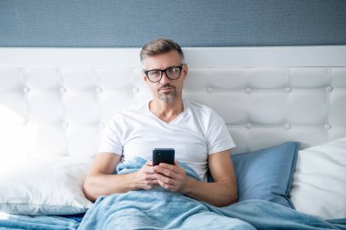 Grizzle adam yatakta gözlüklü telefonla konuşuyor.