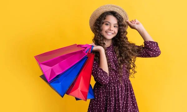 Smiling kid with curly hair hold shopping bags on yellow background — Stock Photo, Image