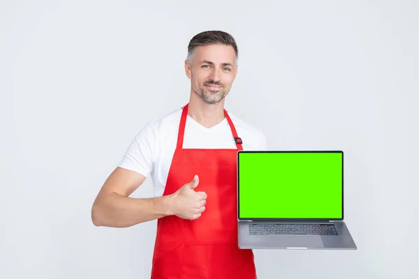 Happy mature man in apron presenting laptop with copy space — Stock Fotó
