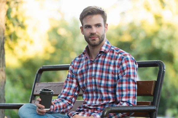 Parktaki bankta kahve fincanı olan kareli tişörtlü genç adam.