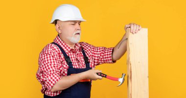 serious aged man woodworker in helmet on yellow background