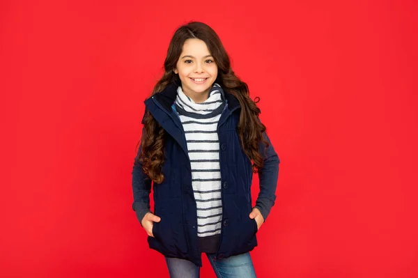 Moda invernale. bambino felice con i capelli ricci in gilet di puffer. teen ragazza su sfondo rosso. — Foto Stock