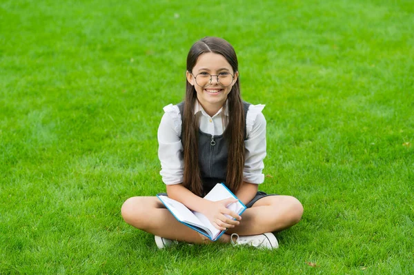 Happy child in glasses reading book sitting on green grass — Fotografia de Stock