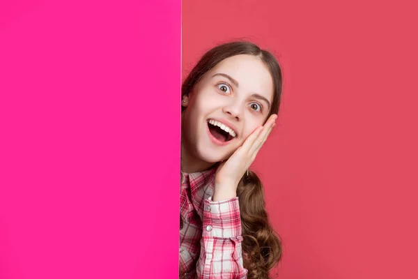 Shocked girl behind blank pink paper with copy space for advertisement — стоковое фото