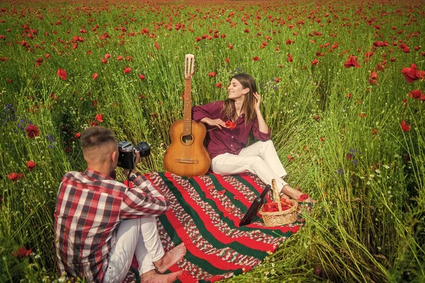 Par kär att göra foto på kameran med akustisk gitarr på sommaren vallmo blomma fält, fritid. — Stockfoto