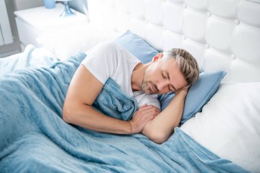 Olgun bir adam yatak odasında uyuyor. Sabah erken saatlerde