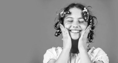 Moda ipuçları. Gençlik hobileri. Kıvırcık saçlı, turuncu saçlı küçük bir kız. Kuaför salonu. Kadın güzellik rutini. Sevimli çocuk saçı. Kafasında bigudilerle gülen kızı.