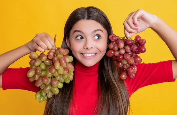 Surprised teen girl hold bunch of grapes on yellow background — Stock Fotó
