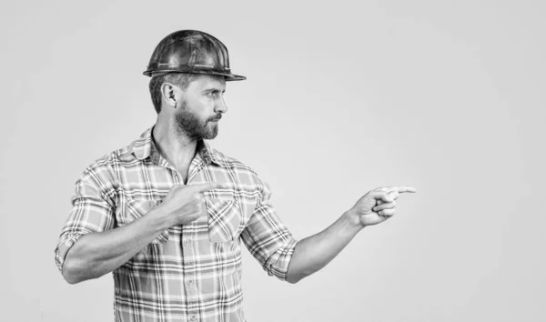 Hombre guapo reparador en la construcción casco de seguridad y camisa a cuadros en el sitio de construcción apuntando finegr, espacio de copia, publicidad —  Fotos de Stock