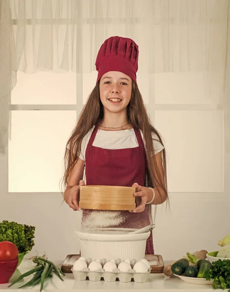 아이들은 집에서 건강에 좋은 음식을 준비하고 요리용 유니폼을 입습니다. 집안일과 집안일을 돕는 일. 아동 발달. 부엌에서 굽는 작은 소녀. 밀가루로 요리하는 꼬마 요리사. 생각이 있는 음식 — 스톡 사진