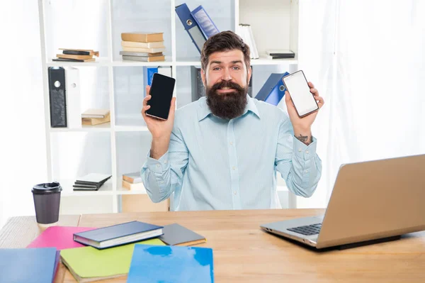 Onnellinen kaveri kädessään matkapuhelimet istuu toimistossa työpöytä, valinta — kuvapankkivalokuva