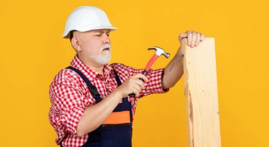 serious old man woodworker in helmet on yellow background