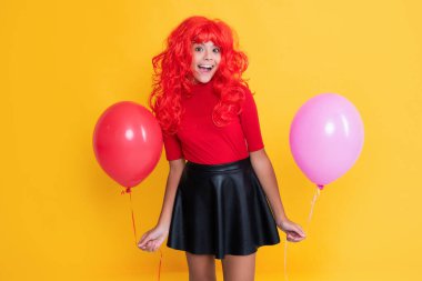 Sarı arka planda parti balonu olan şaşkın genç çocuk.