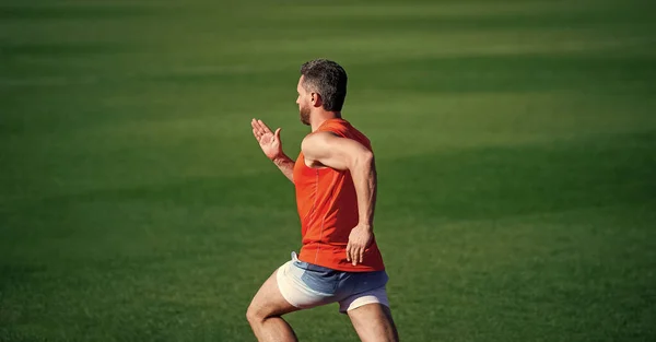 Enérgico atlético musculoso hombre corredor corriendo al aire libre en verde hierba, trotando — Foto de Stock