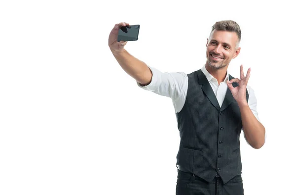 Glücklicher Manager in Anzugweste zeigt OK Ring Geste Selfie mit Smartphone isoliert auf weiß — Stockfoto