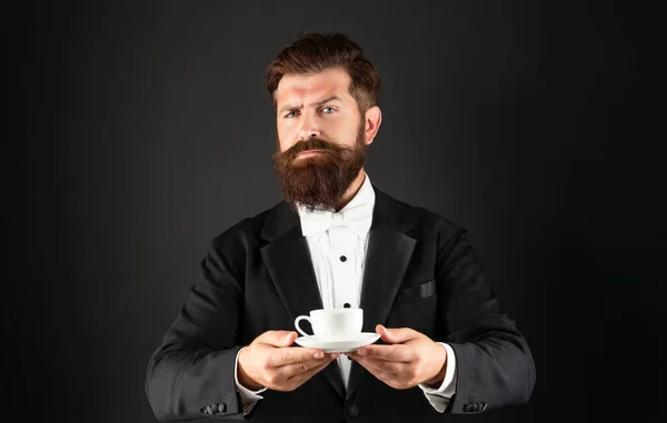 Brutale uomo in smoking papillon con tazza di caffè. cameriere in abiti formali che serve caffè — Foto Stock