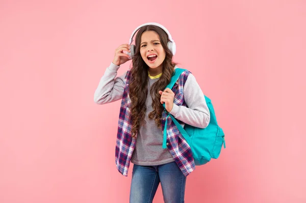 Kid listening loud music in earphones with school bag on pink background, back to school — Stock Fotó