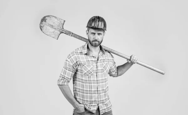 Красивый мужчина работает в шлеме безопасности строительства и клетчатой рубашке на строительной площадке с лопатой, промышленности — стоковое фото
