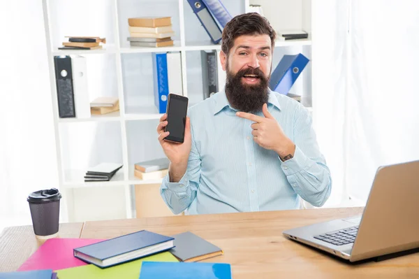 Happy businessman pointing finger at smartphone sitting at office desk, mobile communication — kuvapankkivalokuva