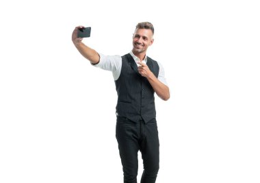 Happy employee in suit vest making videochat pointing finger at smartphone isolated on white