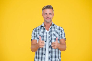 Sarı arka planda kır saçlı mutlu olgun bir adam. başparmak yukarı