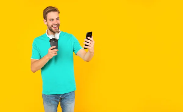 Happy unshaven young man drink coffe and making selfie on phone on yellow background, communication — Fotografia de Stock