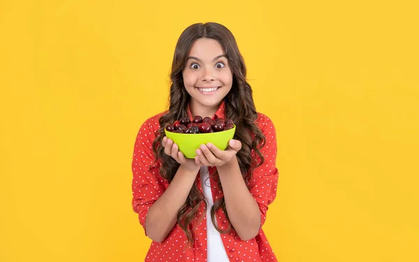 Zaskoczony nastolatek dziewczyna trzymać cherry bowl na żółtym tle — Zdjęcie stockowe
