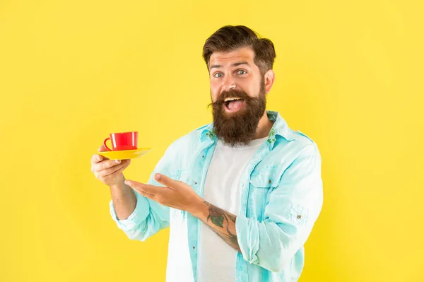 Κατάπληκτος hipster με γενειάδα παρουσίαση φλιτζάνι καφέ σε κίτρινο φόντο, ποτό — Φωτογραφία Αρχείου
