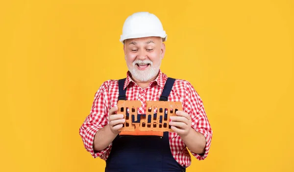 Smiling senior man worker in helmet on yellow background — Stockfoto
