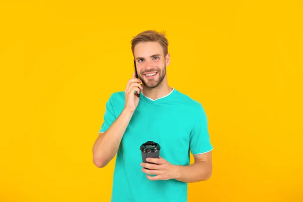 Happy guy with coffee speak on phone on yellow background, conversation — Zdjęcie stockowe