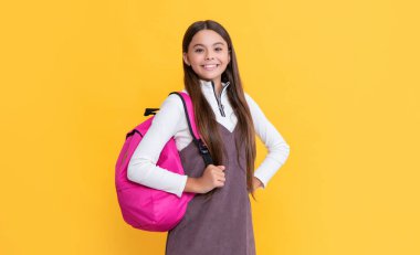 Sarı arka planda okul çantalı mutlu çocuk.