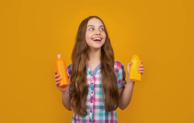 Sarı arka planda şampuan şişesi olan şaşkın çocuk.