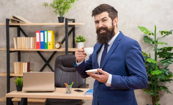 Счастливый бородатый бизнесмен пьет кофе в офисе с копировальным пространством, бизнесмен — стоковое фото