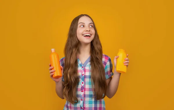 Amazed child with shampoo bottle on yellow background — стоковое фото