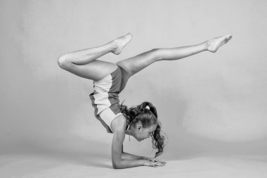 Çocuğun esnek bir vücudu var. Spor kıyafetleri giymiş bir çocuk. Esneme ve ısınma kavramı. çocukluk mutluluğu. Sağlık ve zindelik. Jimnastik. Amuda kalkmış mutlu genç kız