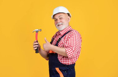 happy old man carpenter in helmet on yellow background. thumb up
