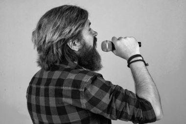 Olgun sakallı adam mikrofonla şarkı söyleyerek modaya uygun görünüyor.