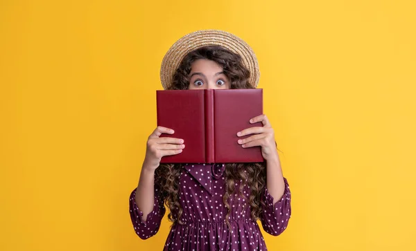 Ragazza felice con i capelli crespi che si nascondono dietro il libro su sfondo giallo — Foto Stock