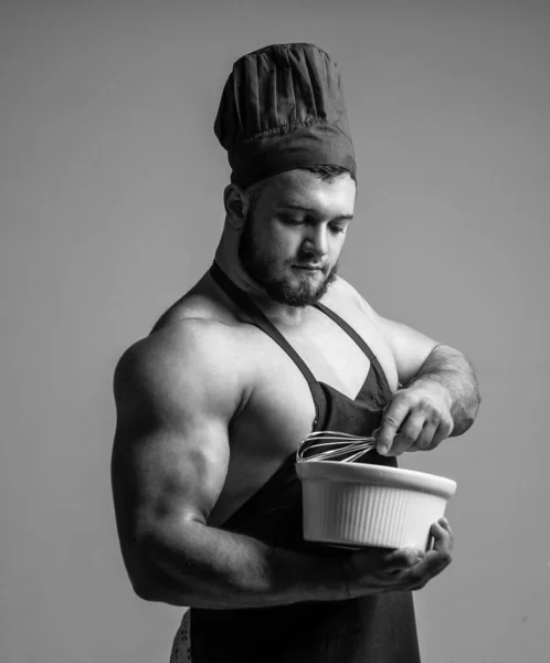 Мускулистый человек готовит в фартуке шеф-повара держать тарелку и битер, готовя пищу — стоковое фото