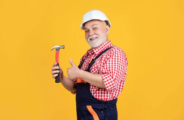 Happy old man carpenter in helmet on yellow background. thumb up — Stockfoto