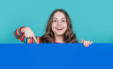 surprised child behind blank blue paper with copy space for advertisement