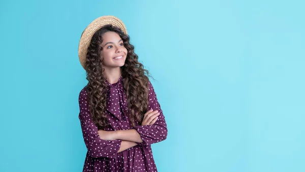 Happy child in straw hat with long brunette curly hair on blue background — Stockfoto