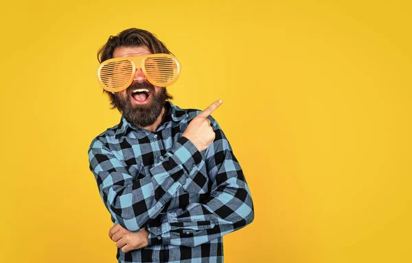 Щасливий бородатий чоловік в смішних партійних окулярах і вказує палець на жовтий фон, копіювати простір, найкраща пропозиція — стокове фото
