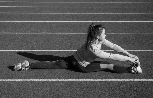 Hon gör sitt bästa. hälsosam barndom. träning på frisk luft utomhus. självsäker löpare. flexibel kropp. Tonårstjejen värmer upp på stadion. Grabben i sportkläder som sträcker sig. barn gör split motion på racing spår — Stockfoto