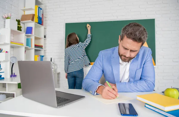 Busy school teacher in classroom with selective focus of kid at blackboard — Stock fotografie