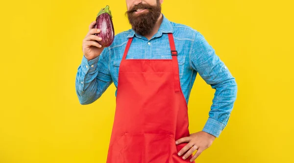 Happy man crop view in red apron holding eggplant yellow background, grocer — Zdjęcie stockowe