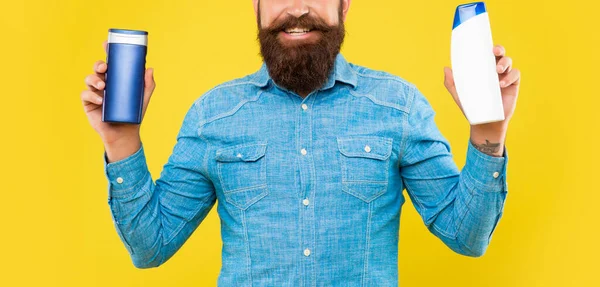 Cropped happy brutal bearded man choosing shampoo bottle on yellow background, presenting toiletries —  Fotos de Stock