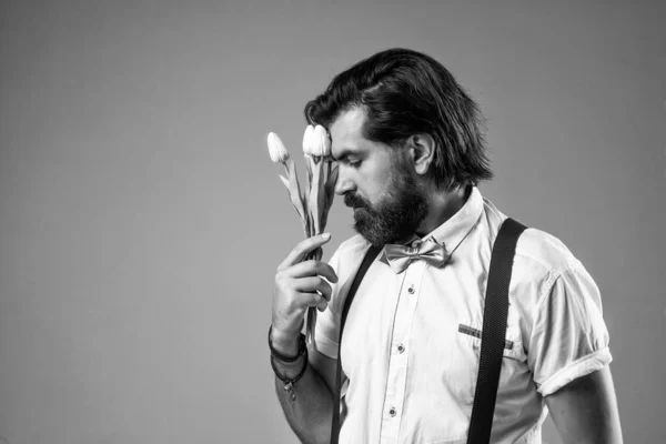 Homme confiant et élégant tenir fleurs de tulipes. cadeau pour la date d'amour. hipster barbu à l'ancienne avec bouquet. fleur de printemps présente. homme romantique en bretelles et noeud papillon. renversé gars — Photo