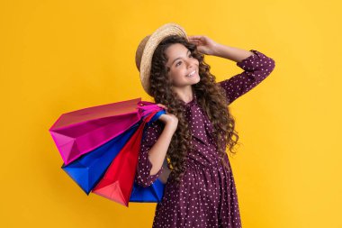 cheerful child with curly hair hold shopping bags on yellow background