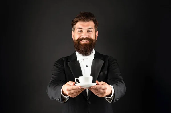 Smokinli, papyonlu, elinde kahve fincanı olan mutlu adam. Siyah arka planda kahve servisi yapan resmi giysili garson. — Stok fotoğraf